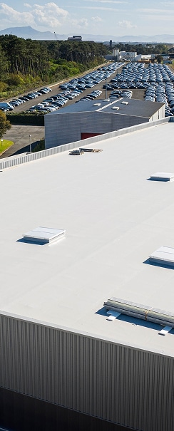 Toit plat blanc d'un entrepôt de distribution automobile Grand toit plat commercial en membrane blanche, surplombant un bâtiment et un immense parking de voitures neuves stockées.