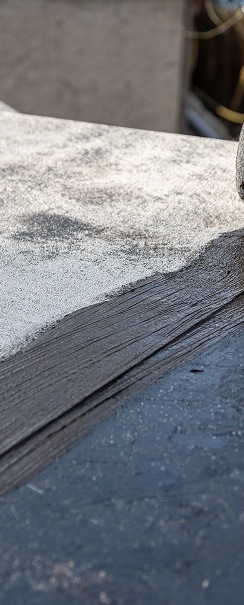 Étanchéité toiture : application d'un revêtement bitumineux. Rénovation de toiture : application d'un revêtement d'étanchéité bitumineux sombre sur une surface granuleuse claire, transition entre neuf et ancien.