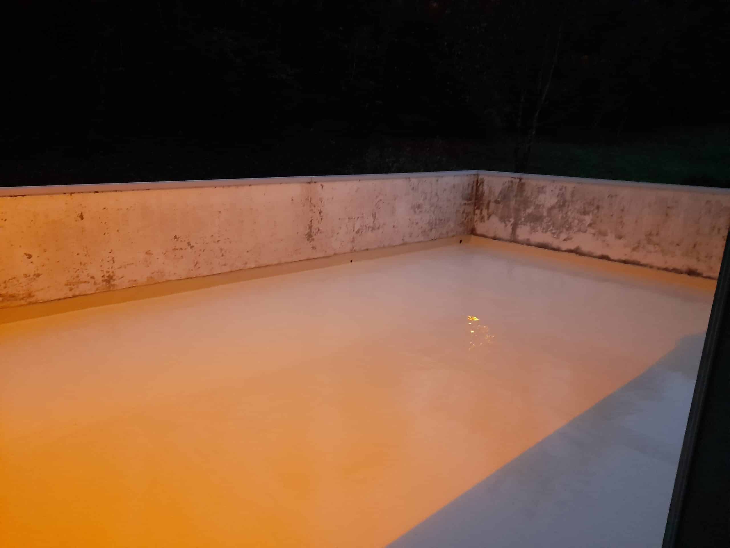 Revêtement de sol étanche pour terrasse : fini lisse orange. Terrasse ou balcon avec un nouveau revêtement de sol lisse, de couleur orange chaud sous un éclairage nocturne. Murs de béton bruts et salis.